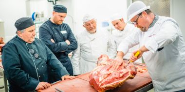Leerkracht slagerij toont cursisten hoe je vlees snijdt