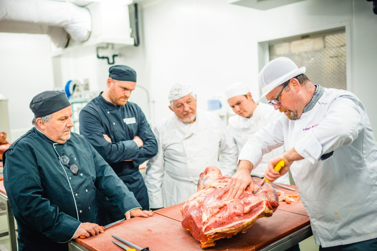 Leerkracht slagerij toont cursisten hoe je vlees snijdt